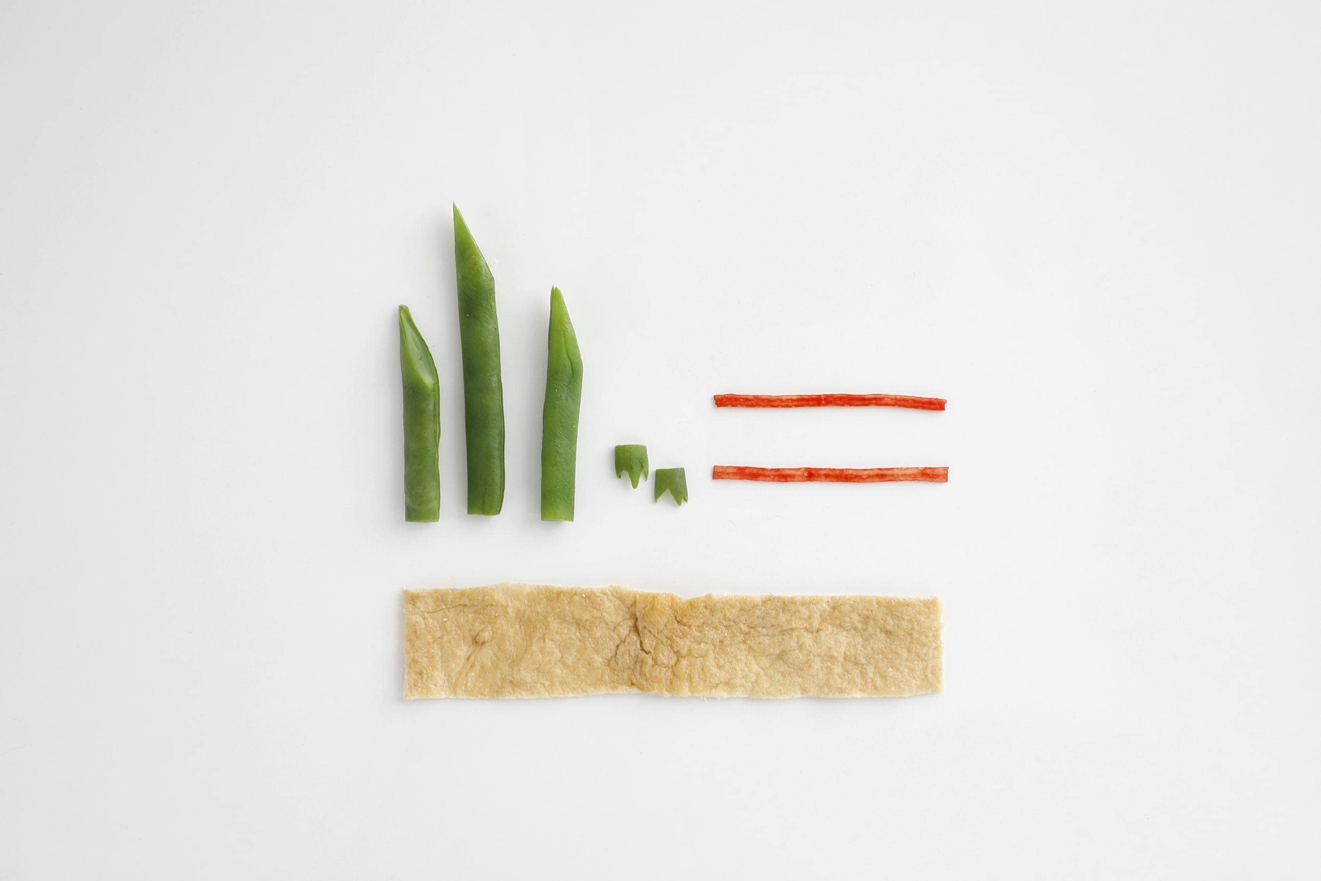 For the green beans, slice the tips diagonally and cut them so there's one long piece and two short ones. Make two tiny crowns with the leftovers. Peel the kamaboko into two thin strips. Cut the aburaage into one long rectangle.